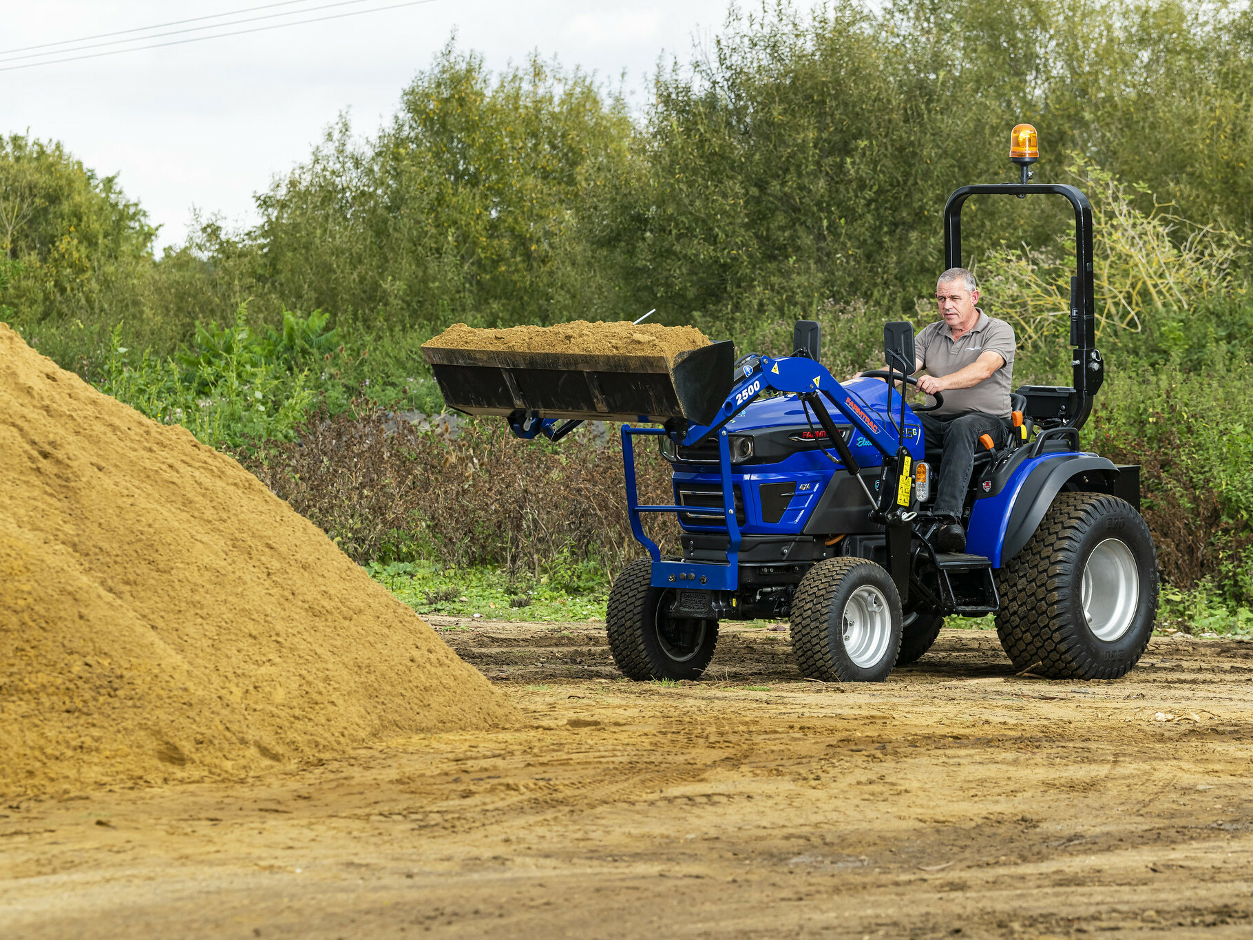 The Farmtrac FT25G being used to transport sand in a front-loader attachment.