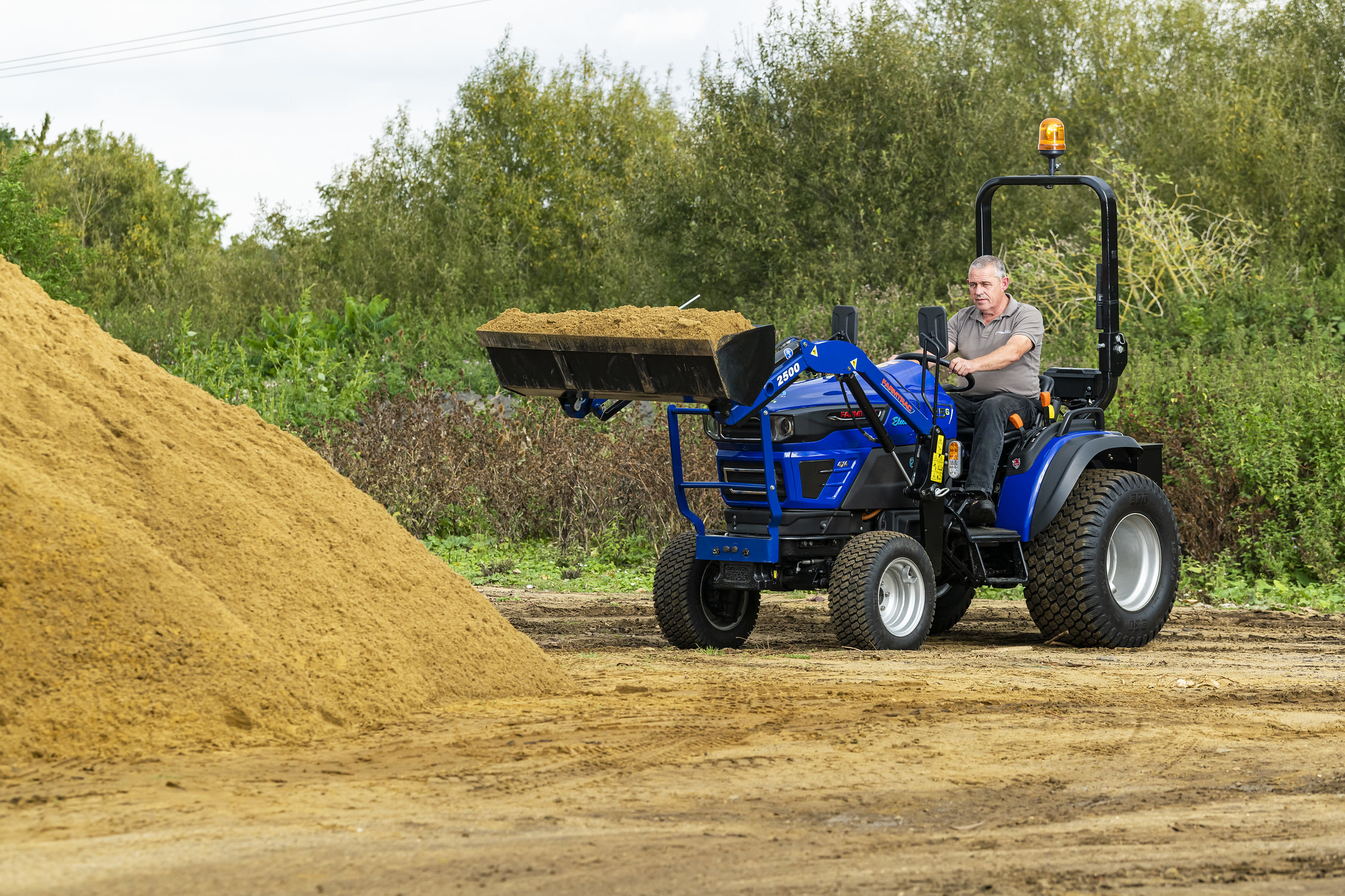 The Farmtrac FT25G being used to transport sand in a front-loader attachment.